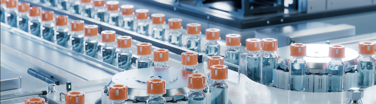 A top-down view of a manufacturing conveyor belt moving rows of glass vials filled with clear liquid and sealed with orange caps, some on straight tracks and others on a circular rotating platform. The bright, cool-toned lighting emphasizes the sterile, precise automation of the process.