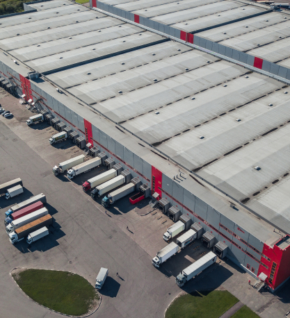 An aerial view of a large logistics warehouse with loading docks and rows of semi-trailer trucks parked at the bays.
